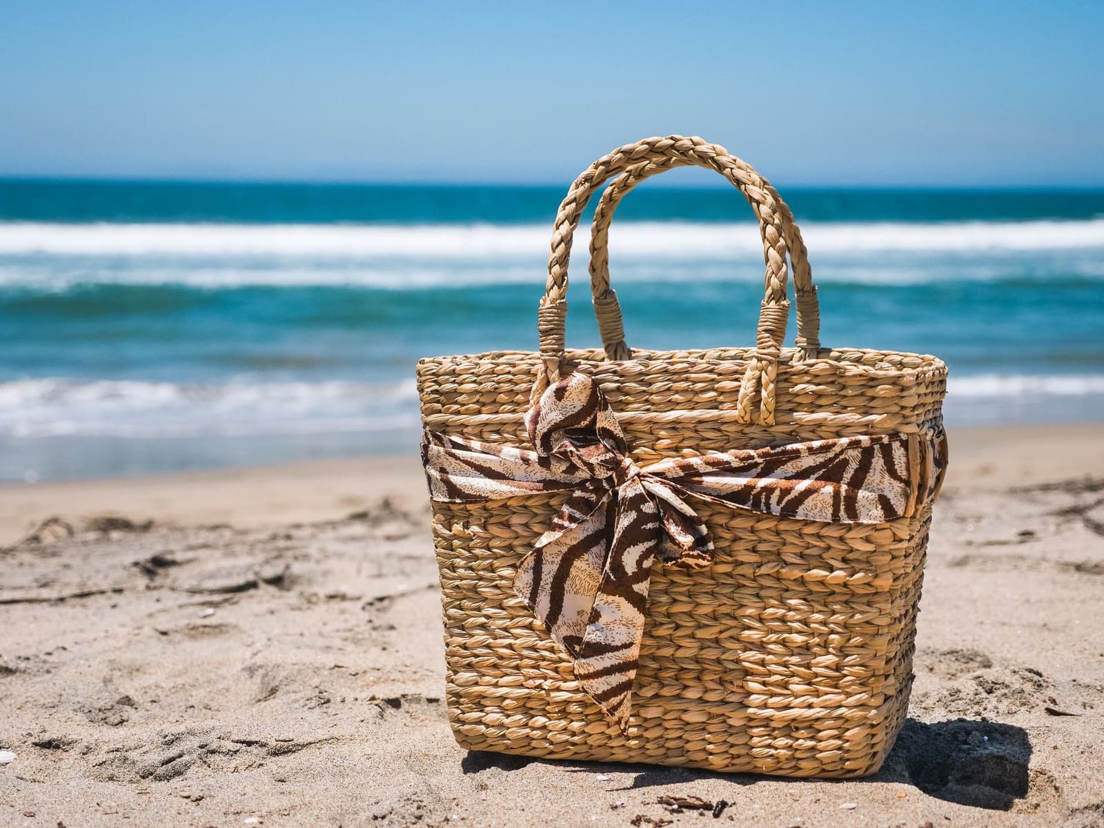 A woven straw bag resting on sunlit sand.