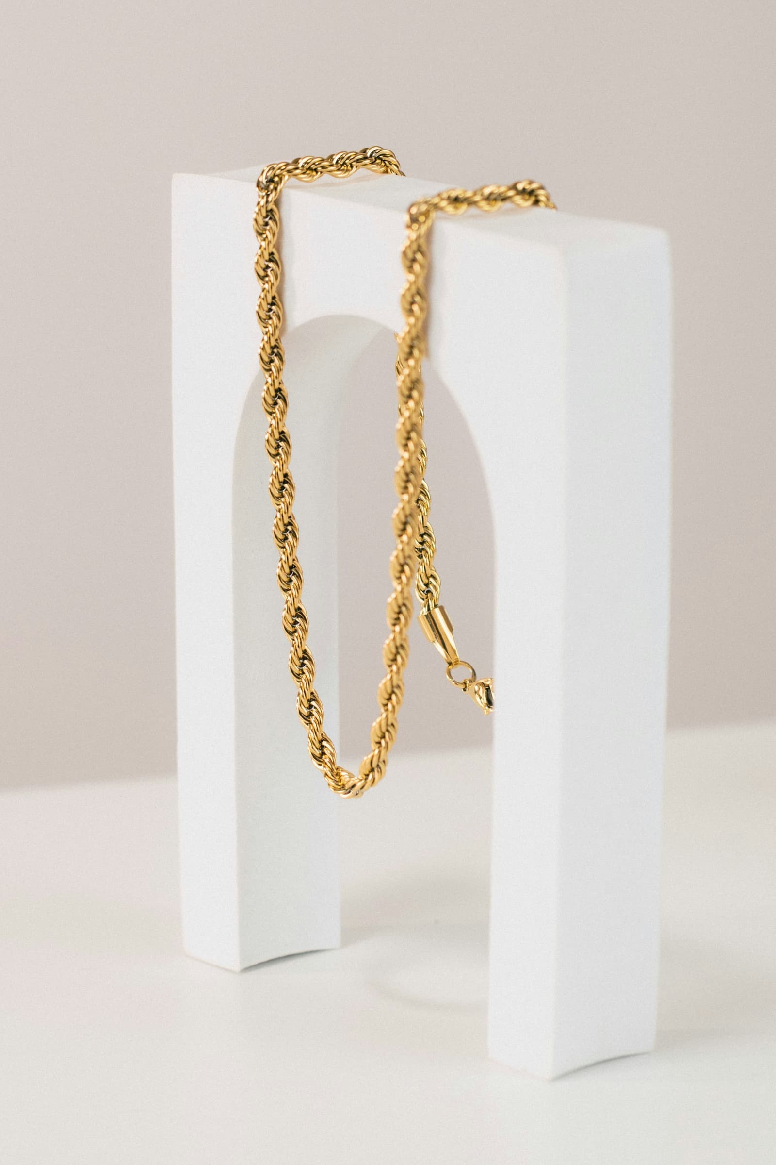 A gold rope necklace on a pale block.