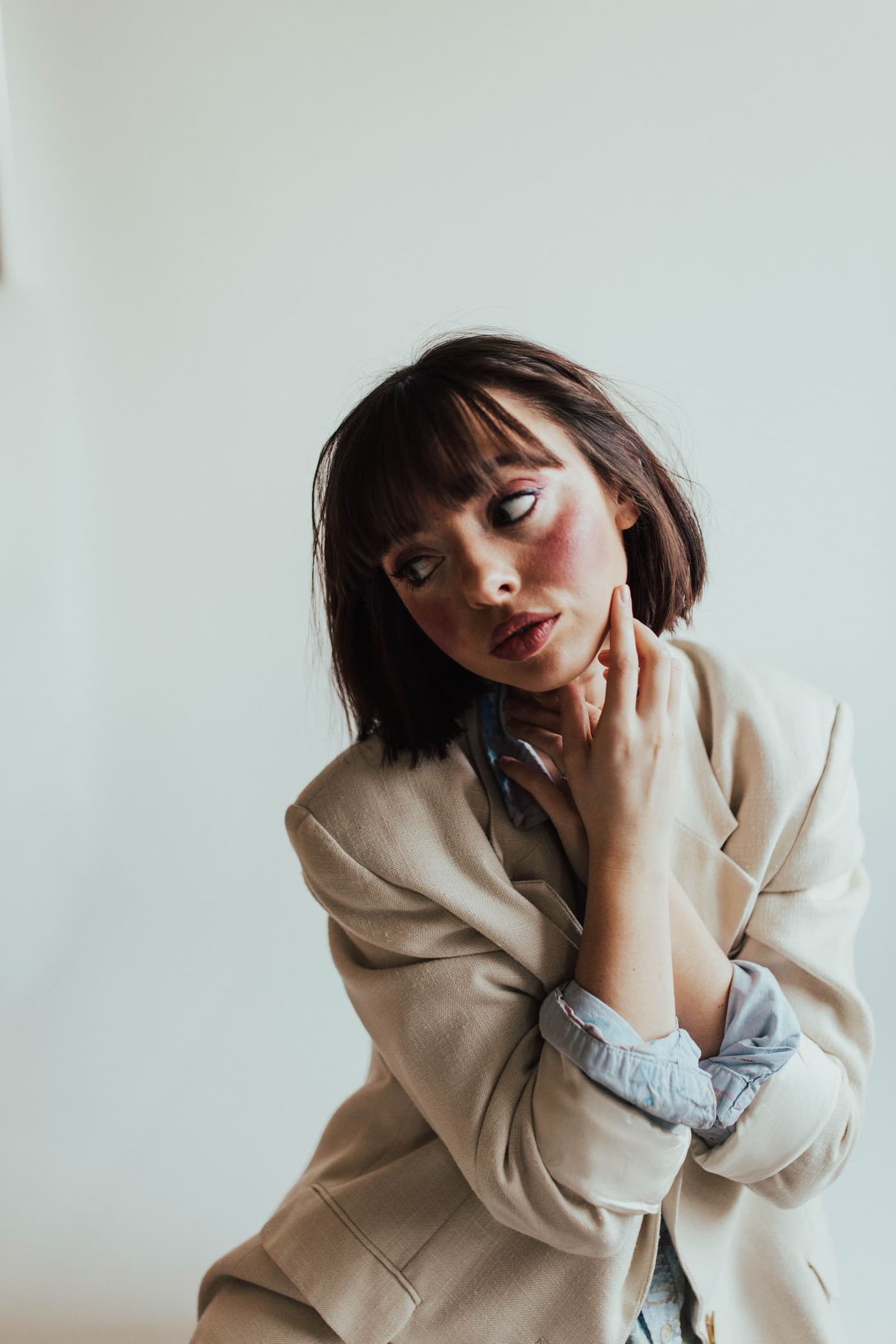 A woman in a beige suit against a white wall.