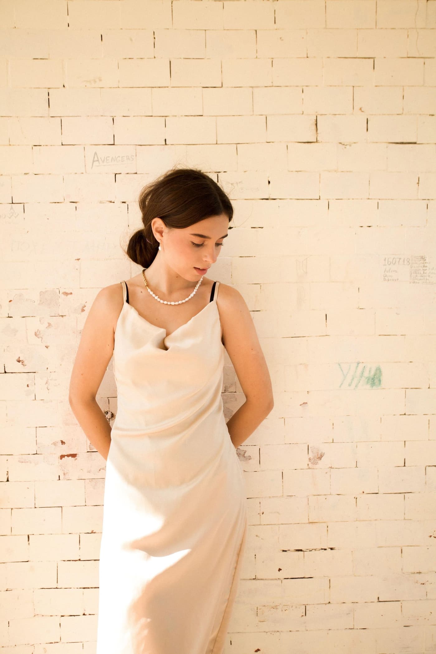 A woman in a beige maxi dress against a warm brick wall.